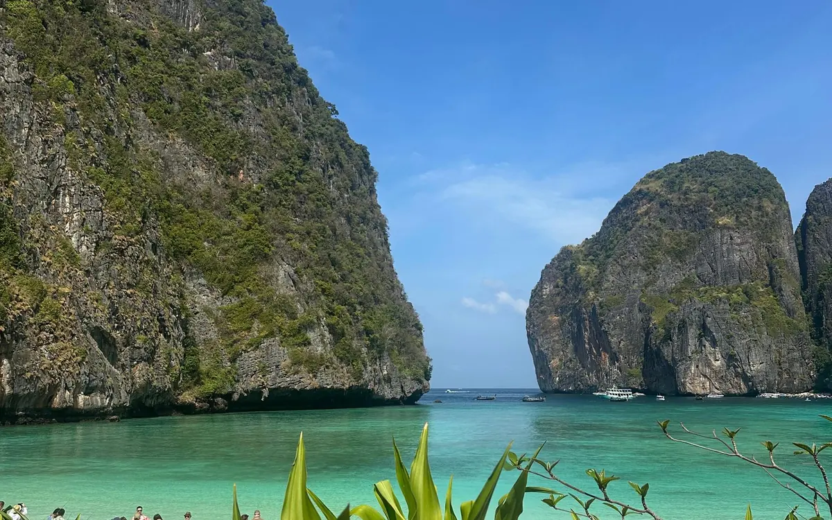 A speedboat crossing open turquoise water towards the limestone cliffs of Phi Phi